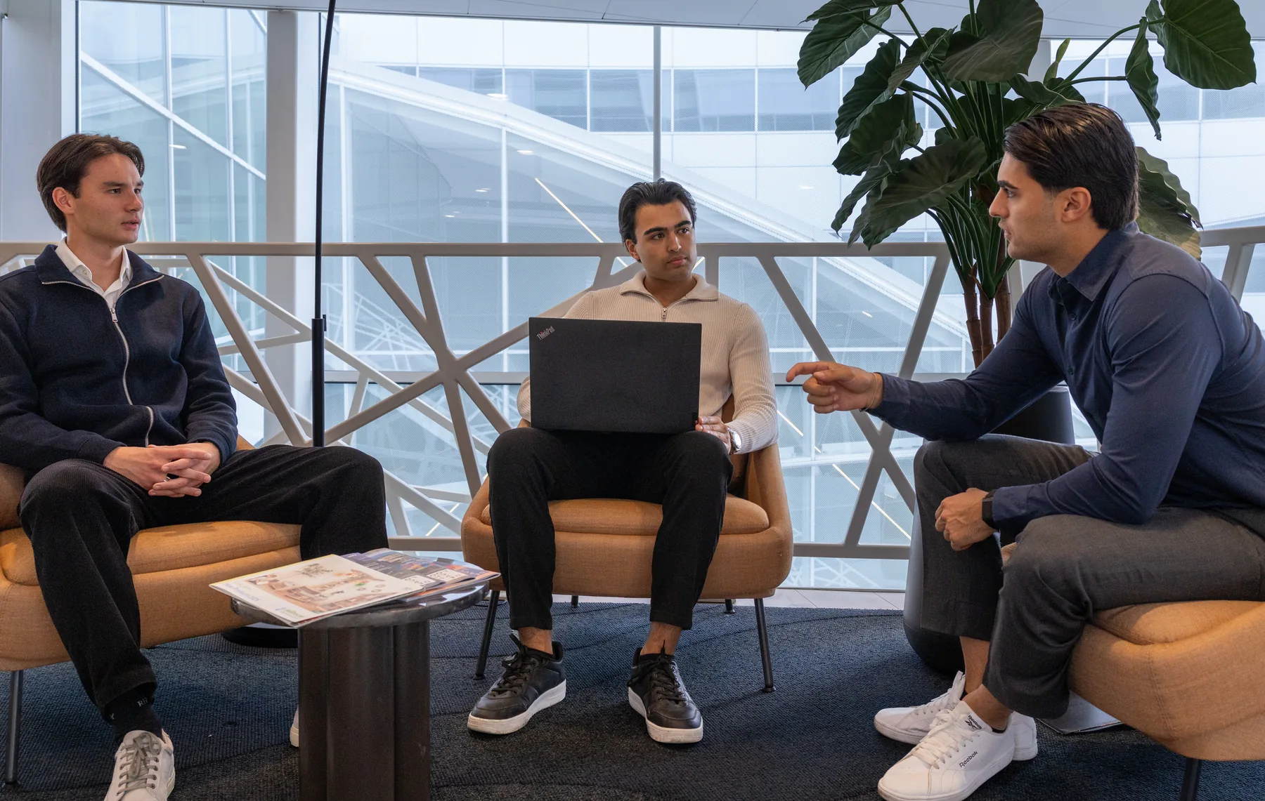 Drie collega’s van Pakr in gesprek, een laptop op schoot